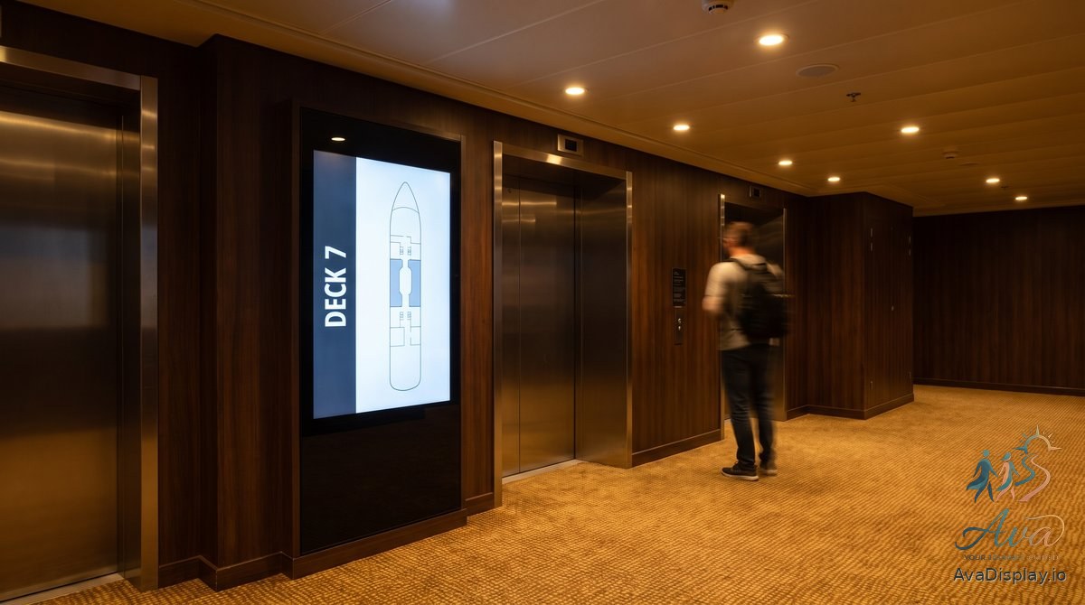 A lit portrait screen beside cruise ship lift doors showing a deck plan